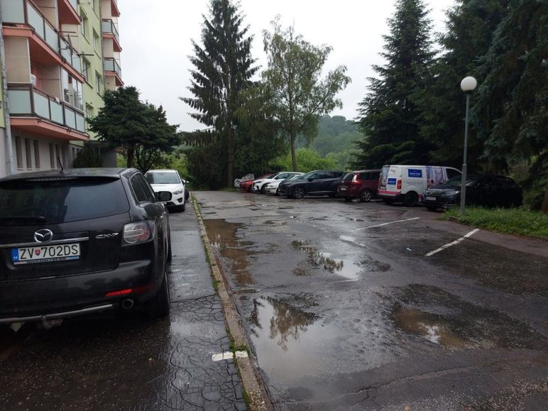 Predaj investičného pozemku. Podborová - Parkovisko na Ružovej ulici v meste Zvolen, obklopené zeleňou a autami.