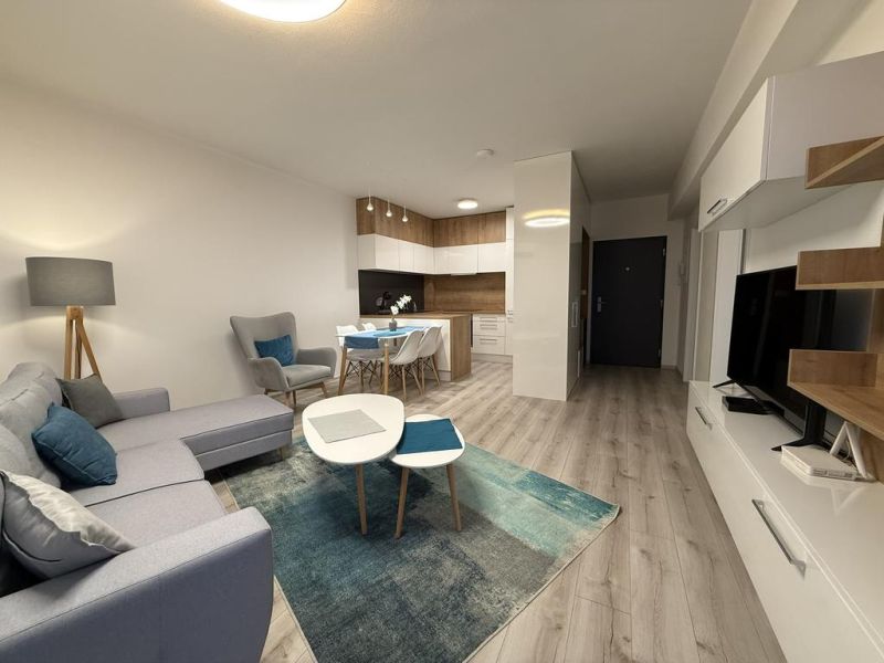 Nové skolaudované byty a apartmány vo Vajnoroch. - Svetlá obývacia izba s kuchynským kútom a podlahou s dreveným dekorom.