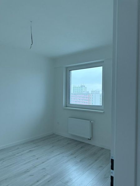 Nové skolaudované byty a apartmány vo Vajnoroch. - Izba s podlahou s dreveným dekorom v 2-izbovom byte, bielymi stenami a radiátorom.