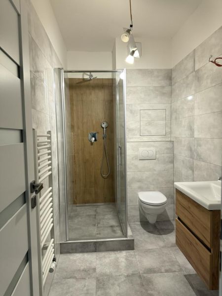Nové skolaudované byty a apartmány vo Vajnoroch. - Kúpeľňa v 2-izbovom byte s dreveným dekorom v sprchovom kúte a rebríkovým radiátorom.