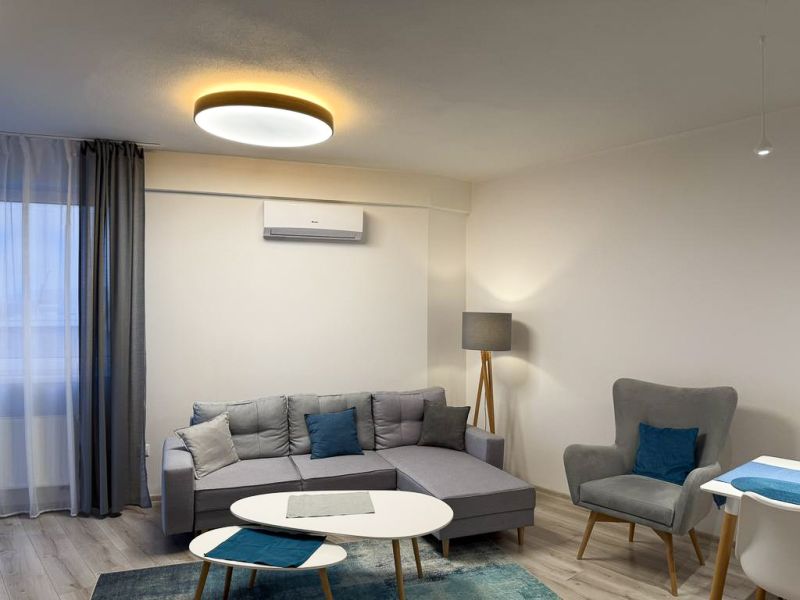 Nové skolaudované byty a apartmány vo Vajnoroch. - Obývacia izba v 2-izbovom byte s podlahou s dreveným dekorom a sivými sedačkami.