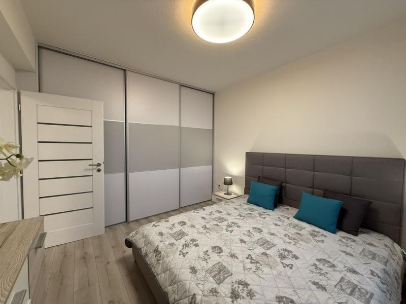 Nové skolaudované byty a apartmány v projekte Diamant. - Spálňa v 2-izbovom byte s posteľou, šatníkovou skriňou a podlahou s dreveným dekorom.