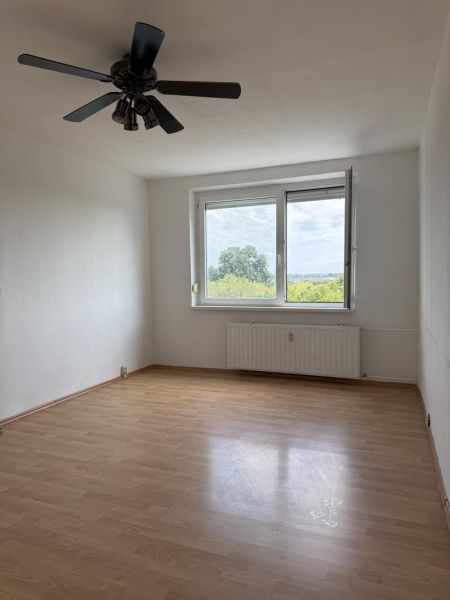 Kľúč RK-Novinka:Priestranný 2-iz.byt s loggiou.(možnosť zmeny na 3-iz) - Izba v 2-izbovom byte s podlahou s dreveným dekorom a stropným ventilátorom.
