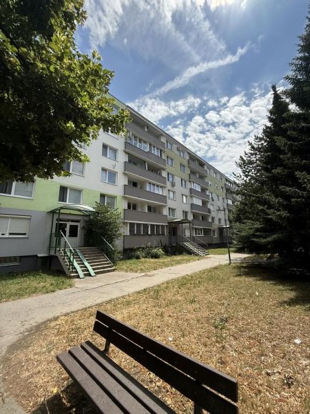 Kľúč RK-Novinka:Priestranný 2-iz.byt s loggiou.(možnosť zmeny na 3-iz) - Bytový dom na Čiližskej ulici v Bratislave-Vrakuni s lavičkou v popredí.