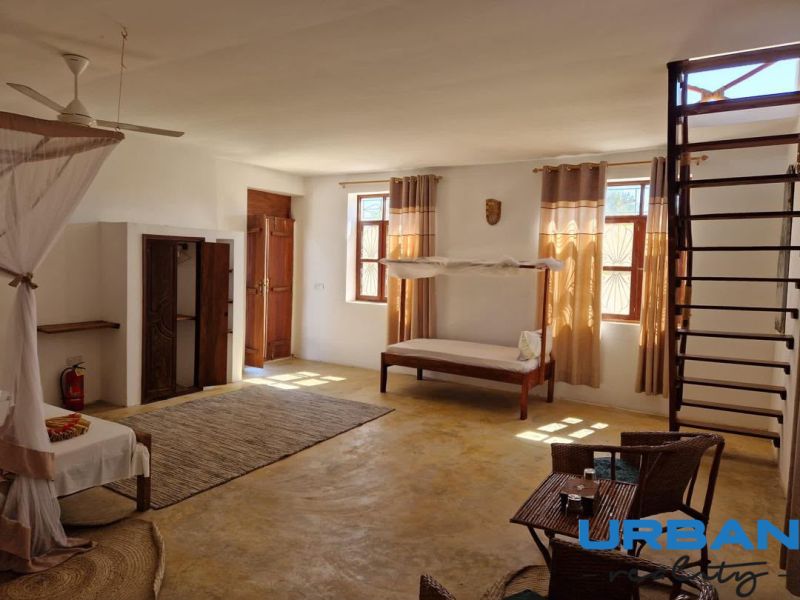 SAMOSTATNE STOJACA VILA MAPUMZIKO S 2 IZBAMI NA ZANZIBARE  - Priestranná izba s posteľou, stoličkami a rebríkom v rodinnom dome.