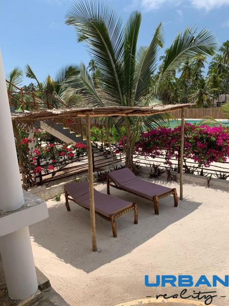 SAMOSTATNE STOJACA VILA MAPUMZIKO S 2 IZBAMI NA ZANZIBARE  - Drevené ležadlá na piesku s palmami a kvetmi v rodinnom dome vo Fumba Town.