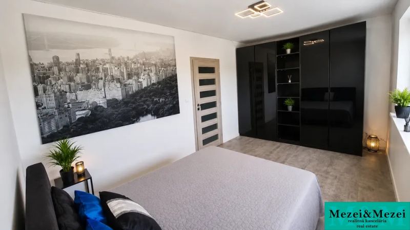 ZARIADENÁ NOVOSTAVBA 5 MINÚT OD TRNAVY - Spálňa s čiernou šatníkovou skriňou, veľkou fotografiou a izbovými rastlinami.