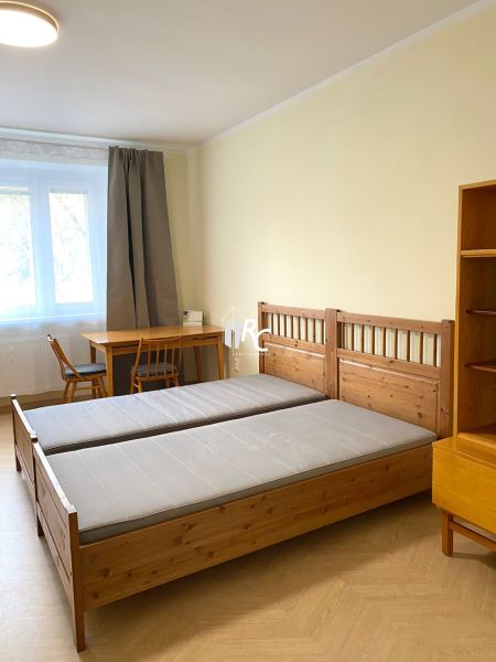 Prenájom 2-izbového bytu, Martin - centrum - Spálňa s drevenými posteľami, stolom a podlahou s dreveným dekorom v 3-izbovom byte.