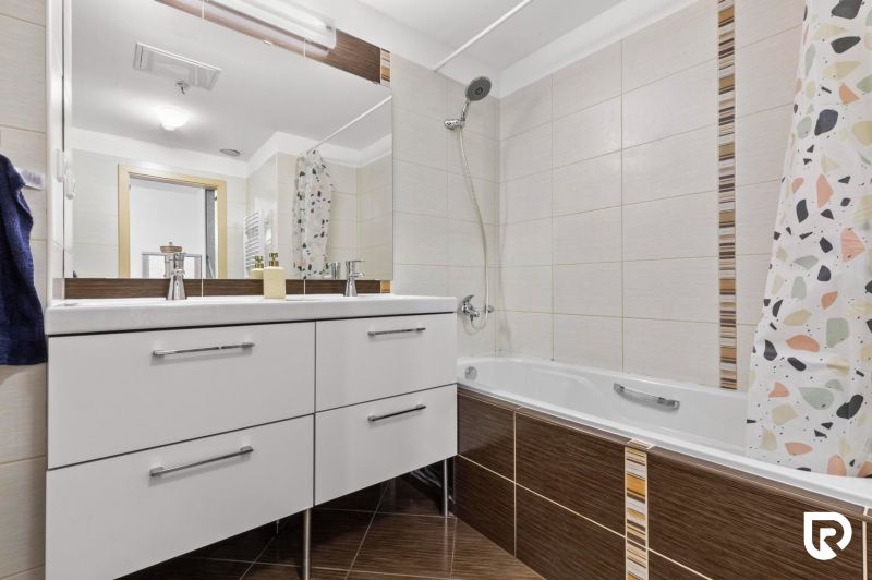 Apartmán vhodný na Airbnb aj rodinné bývanie | Vienna Gate - Kúpeľňa s vaňou v 3-izbovom byte, biele skrinky, dlažba a sprchový záves.