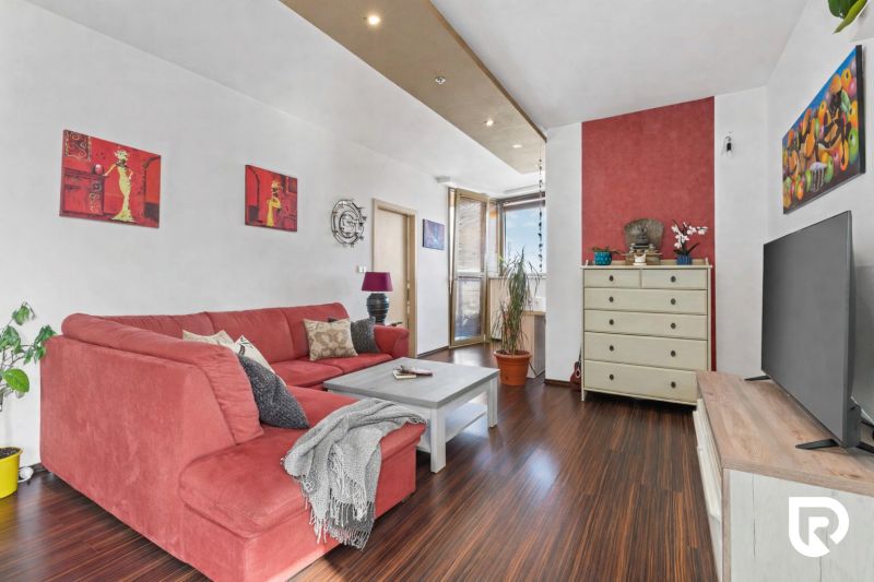 Apartmán vhodný na Airbnb aj rodinné bývanie | Vienna Gate - Obývacia izba s červenou pohovkou a podlahou s dreveným dekorom v 3-izbovom byte.