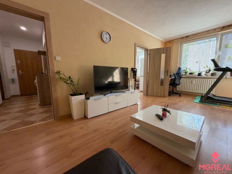 3 izbový byt s balkónom Topoľčany  - Obývačka v 3-izbovom byte s podlahou s dreveným dekorom, televíziou a bežeckým pásom.