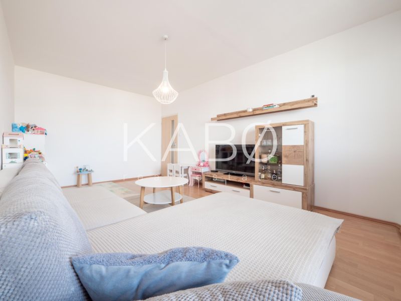 Klimatizácia | Výhľad na Zobor | Balkón a Komfortná veľkosť - Svetlá obývačka s veľkou sedačkou, podlaha s dreveným dekorom, útulný 2-izbový byt.