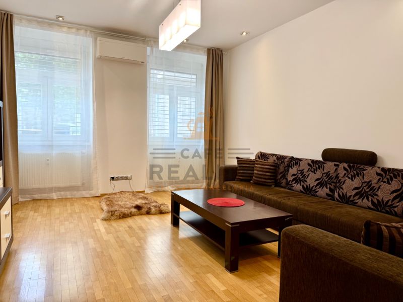 Na prenájom 2 izbový byt, 65 m2, Bratislava, centrum, Vajanského nábr. - Obývacia izba s drevenou podlahou a hnedou sedačkou v 2-izbovom byte.