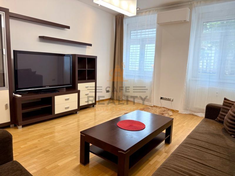 Na prenájom 2 izbový byt, 65 m2, Bratislava, centrum, Vajanského nábr. - Obývacia izba v 2-izbovom byte s pohovkou, televízorom a dreveným nábytkom.