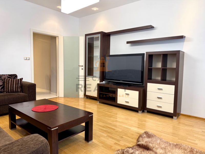 Na prenájom 2 izbový byt, 65 m2, Bratislava, centrum, Vajanského nábr. - Obývačka s hnedou posteľou, dreveným stolíkom a televízorom v 2-izbovom byte.