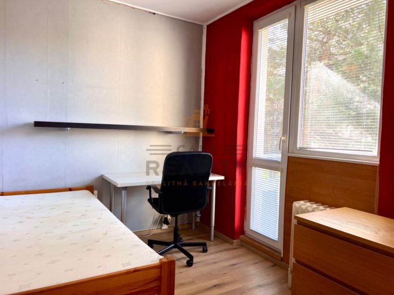 Na predaj 2 izbový byt, 47 m2, Bratislava, Nové Mesto, Piešťanská ul. - Izba v 2-izbovom byte s podlahou s dreveným dekorom, písacím stolom a posteľou.