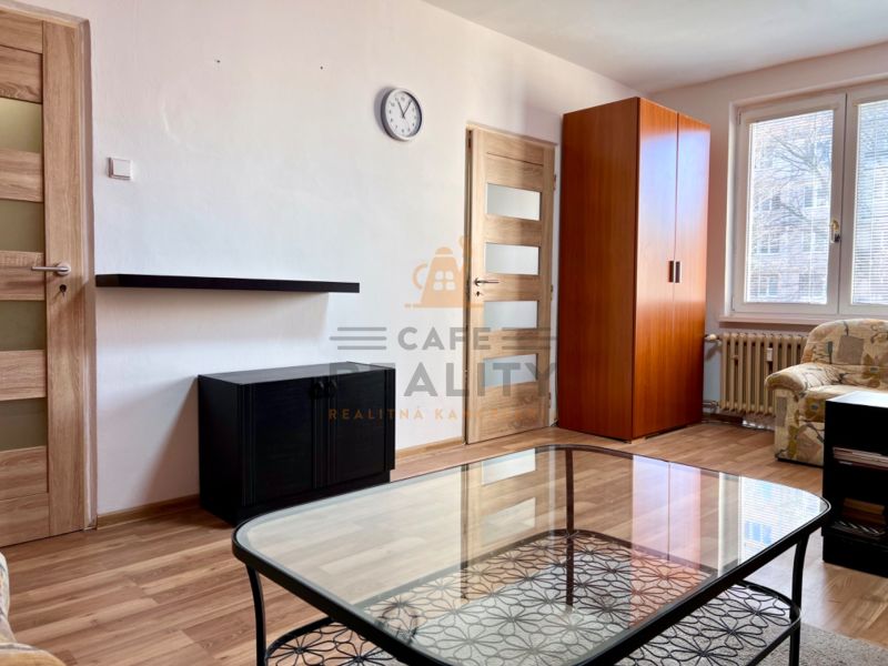 Na predaj 2 izbový byt, 47 m2, Bratislava, Nové Mesto, Piešťanská ul. - Obývacia izba v 2-izbovom byte s podlahou s dreveným dekorom, pohovkou a skriňou.
