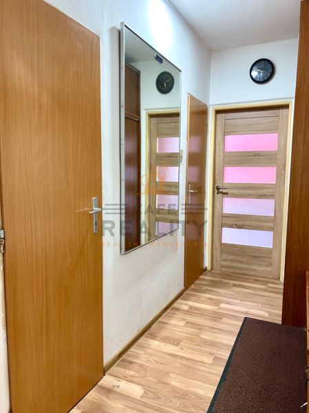 Na predaj 2 izbový byt, 47 m2, Bratislava, Nové Mesto, Piešťanská ul. - Chodba s podlahou s dreveným dekorom v 2-izbovom byte, zrkadlo a hodiny na stene.