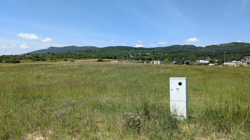 Stavebný pozemok 681 m2 v Štitároch  - Rozľahlé zelené pole s viditeľnou budovou a kopcami v Štitároch na Zamoyského, Pozemky - bývanie.