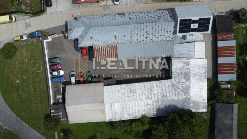 Priemyselný areál (tri haly, recepcia, kancelária, garáže, logistika) - Areál skladov a hál v Banskej Bystrici so zaparkovanými autami a solárnymi panelmi na streche.