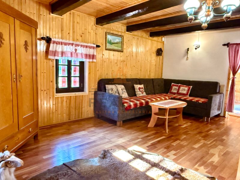 Na predaj chalupa, pozemok 1891 m2, obec Šumiac, okr. Brezno - Interiér rodinného domu s rohovou sedačkou, skrinkou a podlahou s dreveným dekorom.
