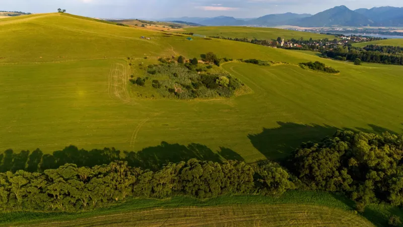 Liptovský Trnovec – 6.488 m2 POZEMOK na MOBILNÝ dom - Zelené lúky a stromy s výhľadom na dedinu v Liptovskom Trnovci, zvláštne nehnuteľnosti.