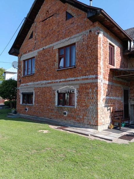 Slnečný pozemok s rodinným domom v Ovčiarsku  - Rodinný dom v Ovčiarsku s neomietnutou tehlovou fasádou a zeleným trávnikom pre pozemky - bývanie.
