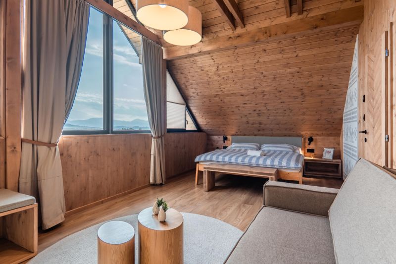 I Luxusné dvojpodlažné chalet pri Liptovskej Mare - Podkrovná izba s veľkým oknom, posteľou, pohovkou a podlahou s dreveným dekorom.