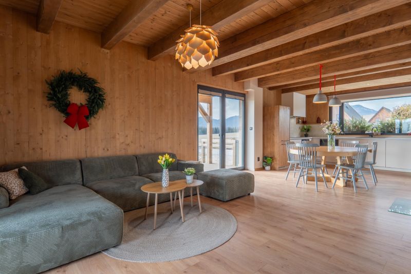 I Luxusné dvojpodlažné chalet pri Liptovskej Mare - Svetlá obývacia izba s kuchyňou, sedačkou, stolom a podlahou s dreveným dekorom.
