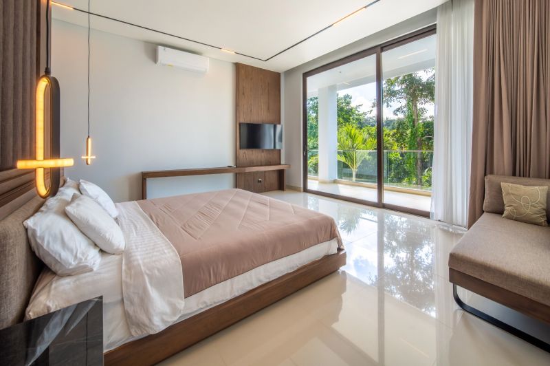 I Na predaj Luxusná vila „Tomma“ v Ubud, Bali - Svetlá spálňa vo vile s posteľou, televízorom a výhľadom na tropickú zeleň.