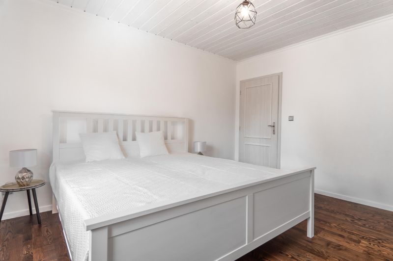 Stavebný pozemok 8 500 m² s podnikateľským potenciálom - Biela spálňa s manželskou posteľou a podlahou s dreveným dekorom.
