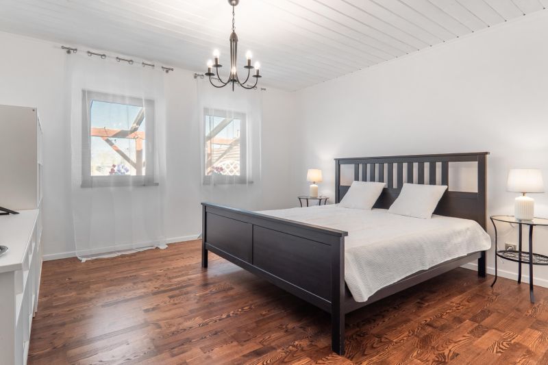 Stavebný pozemok 8 500 m² s podnikateľským potenciálom - Spálňa s posteľou, podlahu zdobí drevený dekor, svetelný luster, záclony na oknách.