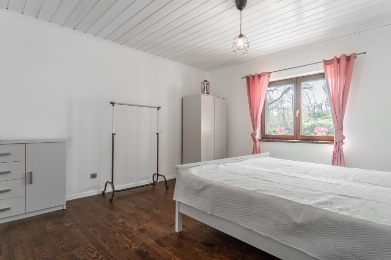 Stavebný pozemok 8 500 m² s podnikateľským potenciálom - Spálňa s ružovými závesmi, veľkým oknom a podlahou s dreveným dekorom.