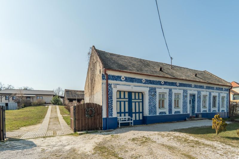 Stavebný pozemok 8 500 m² s podnikateľským potenciálom - Tradičný modrobiely dom na bývanie v Dolnom Lopašove, obklopený zelenými pozemkami.