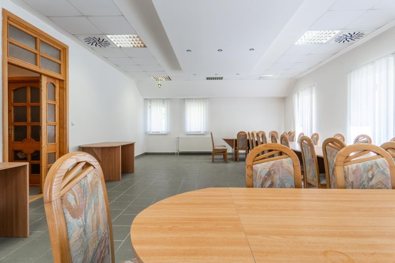 I PREDAJ – FUNGUJÚCA PEKÁREŇ A POTRAVINY V TRNAVE - Priestranná miestnosť s drevenými stolmi a stoličkami, neutrálna farebná paleta.
