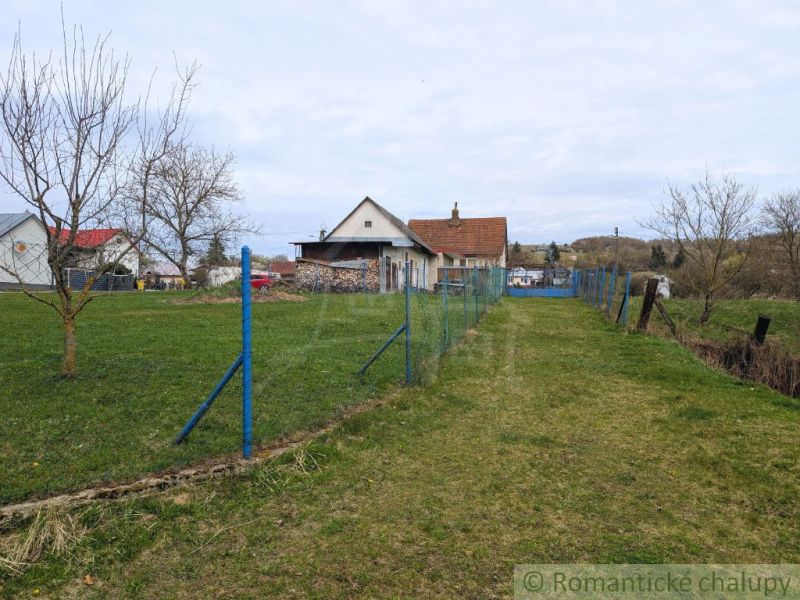 Útulný dom na bývanie alebo chalupu bez susedov a veľkým pozemkom - Rodinný dom v obci Volica s trávnikom a modrým plotom, bez lístia na stromoch.