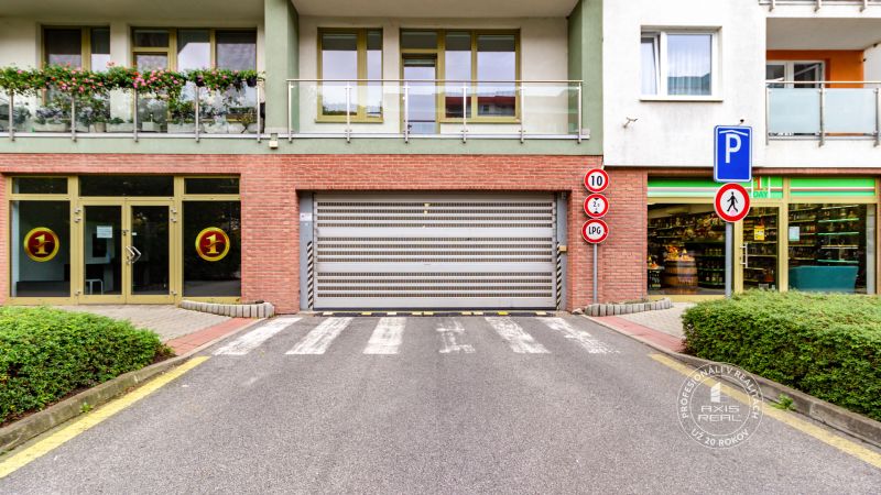 UZAMYKATEĽNÁ GARÁŽ 20m2 v NOVOSTAVBE Vodotika, Lužná ul. - Garáže na Lužnej ulici v Bratislave-Petržalke s rampou a obchodom v pozadí.