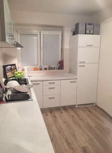 Prerobený 2 izbový byt v centre mesta Nové Zámky - Kuchyňa v 2-izbovom byte s bielymi skrinkami a podlahou s dreveným dekorom.