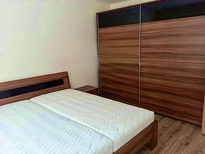 Prerobený 2 izbový byt v centre mesta Nové Zámky - Spálňa v 2-izbovom byte s posteľou a veľkou skriňou, podlaha s dreveným dekorom.