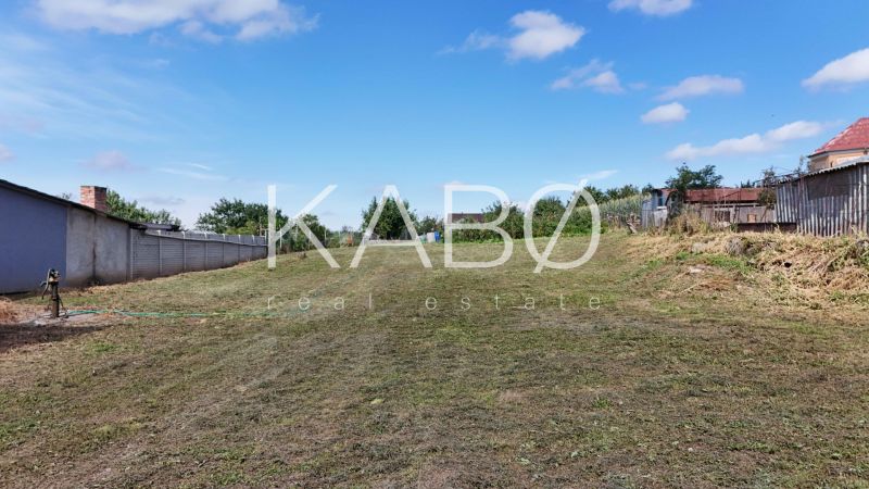 Stavebný pozemok 1 750 m² v centre obce Rumanová - Pozemok na bývanie v Rumanovej, tráva, plot, záhrada, jasná obloha.