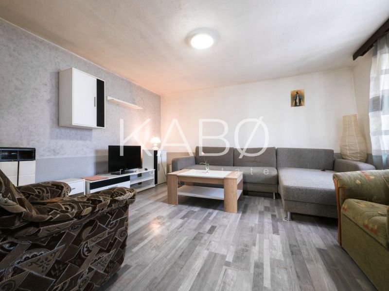 3 izbový Rodinný dom v Cabaj-Čápore s pozemkom 1 053 m² - Obývacia izba s kobercami, sedačkou, televíziou a podlahou s dreveným dekorom v rodinnom dome.