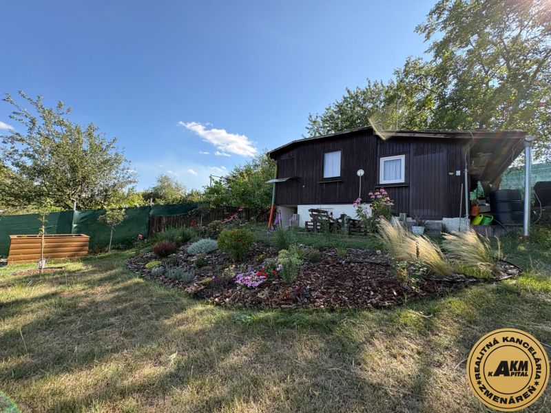  Záhrada -  Zlatý potok na Predaj - Záhrady v Zvolene s drevenou chatou, okrasnými kvetinami a zeleňou pod modrou oblohou.