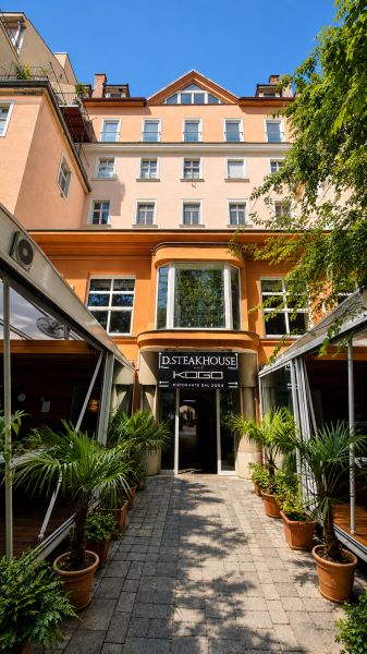Diamant medzi apartmánmi v srdci Starého mesta - Reštaurácia na Hviezdoslavovom námestí v Bratislave - Starom Meste, obklopená zeleňou a palmami.