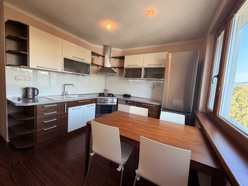 NOVINKA!!! Priestranný 3-izbový byt, 72 m² | Karpatská, Sásová - Kuchyňa s bielymi skrinkami, podlaha s dreveným dekorom a jedálenský stôl.