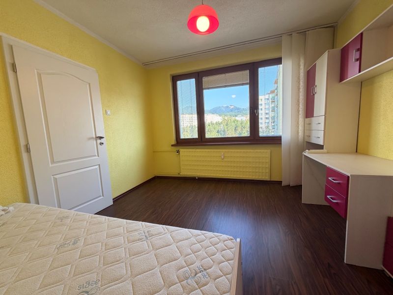 NOVINKA!!! Priestranný 3-izbový byt, 72 m² | Karpatská, Sásová - Žlté steny izby s podlahou s dreveným dekorom v 3-izbovom byte.