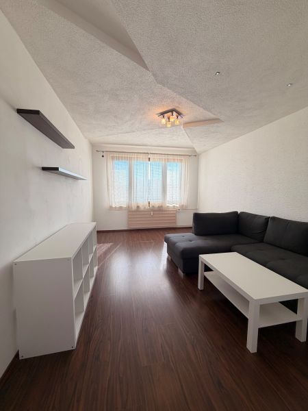 NOVINKA!!! Priestranný 3-izbový byt, 72 m² | Karpatská, Sásová - Obývačka v 3-izbovom byte s podlahou s dreveným dekorom a rohovou sedačkou.