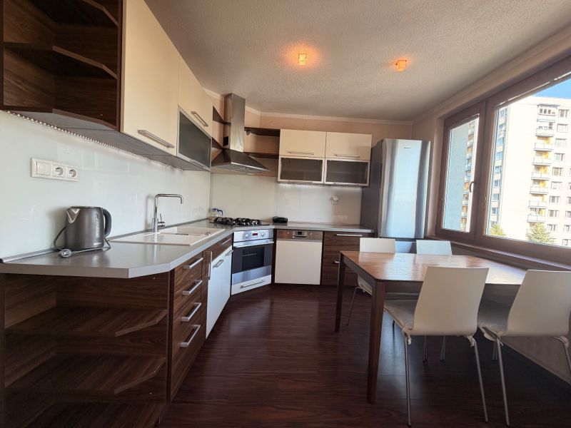 NOVINKA!!! Priestranný 3-izbový byt, 72 m² | Karpatská, Sásová - Kuchyňa v 3-izbovom byte s podlahou s dreveným dekorom a jedálenským stolom.