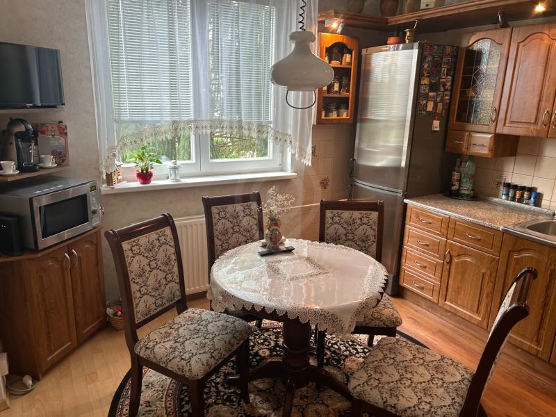 NA PREDAJ PRIESTRANNÝ 3-IZBOVÝ BYT | 67 m² | LODŽIA | 4. POSCHODIE - Kuchyňa v 3-izbovom byte s podlahou s dreveným dekorom a čipkovaným obrusom na stole.