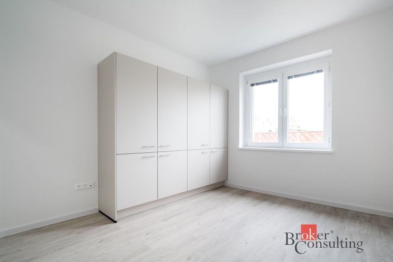 Na predaj : Kompletne zrekonštruovaný 3-izbový byt na Štúrovej v Nitre - Svetlá izba s bielou skriňou a podlahou s dreveným dekorom v 3-izbovom byte.