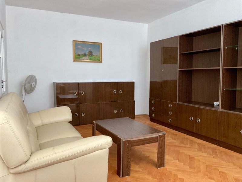 I PREDAJ 2-IZBOVÝ BYT S KLIMATIZÁCIOU A BALKÓNOM I RUŽINOV - Obývacia izba v 2-izbovom byte s podlahou s dreveným dekorom, sofou a skrinkami.